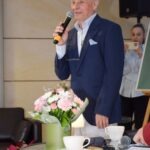 Mężczyzna w garniturze przemawia do publiczności, trzymając mikrofon.