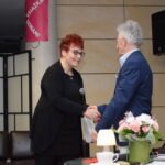 Dwóch rozmówców podaje sobie ręce podczas wydarzenia.