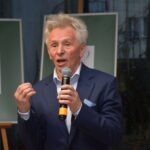 Mirosław Janik, w marynarce, mówi do mikrofonu podczas wystąpienia.