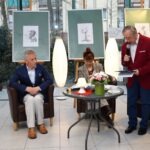 Mężczyźni rozmawiają w fotelu i przy stole, a kobieta siedzi obok nich podczas spotkania.