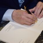 Mężczyzna w garniturze podpisywał dokument piórem z pozłacanym uchwytem.