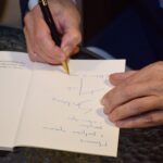 Osoba pisze długopisem na otwartym notatniku.