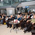 Uczestnicy zebrani są w sali, siedząc na krzesłach wokół stolika z napojami podczas spotkania Akademii Słowa.