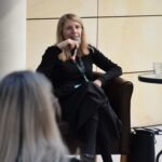 Prelegentka siedzi na krześle i prowadzi dyskusję podczas panelu ChrzanCon w bibliotece.