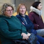 Trzy kobiety siedzą obok siebie na krzesłach podczas wydarzenia w bibliotece.