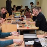 Uczestnicy skupieni przy długim stole biorą udział w maratonie gier planszowych podczas ChrzanConu.