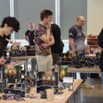 Uczestnicy wydarzenia ChrzanCon oglądają ekspozycję gier planszowych na stole w bibliotece.