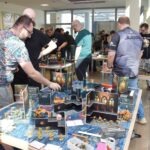 Uczestnicy rozgrywki planszowej skupieni nad modelem terenu przedstawiającym strukturę podziemną.