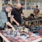 Uczestnicy rozgrywki planszowej skupiają się nad modelem terenu z elementami architektonicznymi.