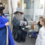 Uczestnicy wydarzenia ChrzanCon w przebraniach elfów i czarodzieja rozmawiają przy stoliku podczas festiwalu.