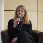 Kobieta siedzi na fotelu i mówi do mikrofonu podczas panelu dyskusyjnego.