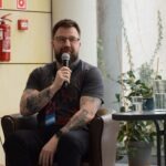 Mężczyzna z brodą trzyma mikrofon podczas panelu dyskusyjnego na wydarzeniu ChrzanCon.