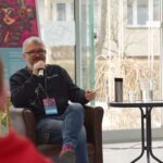 Mężczyzna z brodą siedzi na krześle podczas panelu dyskusyjnego na ChrzanConie.