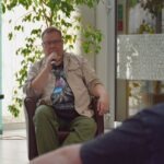 Mężczyzna siedzi na krześle i mówi do mikrofonu podczas panelu dyskusyjnego.