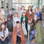 Grupa dzieci i młodzieży w kostiumach postaci z fantasy pozuje do zdjęcia w bibliotece podczas ChrzanConu.