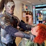 Uczestnik ChrzanCon w kostiumie wojownika z mieczem pochyla się nad fryzjerem podczas strzyżenia.