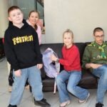 Uśmiechnięta rodzina siedzi na sofie, a chłopiec w czarnym dresie ma nałożone kolorowe skarpetki.