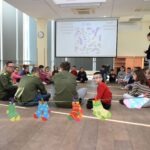 Przedszkolaki siedzą na podłodze w sali podczas warsztatów, a przed nimi leżą zabawki.