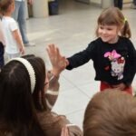 Dziecko wyciąga rękę do osoby siedzącej naprzeciwko podczas wydarzenia w bibliotece.