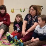 Dzieci siedzą w kręgu podczas spotkania, a jedna z nich ma kolorowe skarpetki.