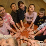Dzieci uczestniczą we wspólnym zajęciu, układając dłonie na drewnianym stole.