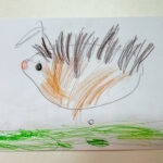 Dziecięca praca przedstawia jeża z pomalowanymi na brązowo i pomarańczowo kolcami oraz zielonymi plamami imitującymi trawę.