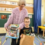 Dziecko i kobieta prezentują nagrodę - zestaw edukacyjny i torbę z upominkami w bibliotece.