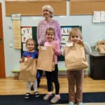 Trójka przedszkolaków prezentuje torby z nagrodami podczas konkursu plastycznego w bibliotece.