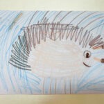 Narysowane kredkami jeżyk ma białe ciało, brązowe kolce i uśmiechniętą twarz.