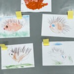 Na szarej tablicy przymocowane żółtymi taśmami znajdują się rysunki jeży wykonane przez dzieci.