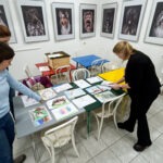 Dzieci i dorosła kobieta przeglądają prace plastyczne wyeksponowane na stole w bibliotece.