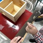 Dziecko trzyma pędzle i składa drewniany element domku dla jeża.