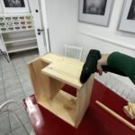 Dziecko przybija gwoździe do drewnianych elementów konstrukcji domku dla jeża.