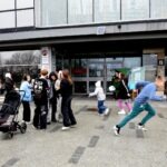 Dzieci z rodzicami uczestniczą w polowaniu na jajka przed budynkiem biblioteki.