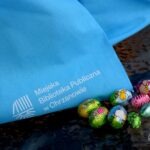 Na okładce książki widnieje napis "Miejska Biblioteka Publiczna im. Czesława Janczaka" oraz logo instytucji, a obok leżą kolorowe pisanki.