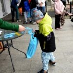 Chłopiec w żółtej kurtce wkłada niebieską torbę na stół podczas polowania na jajka wielkanocne.