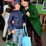 Chłopiec w niebieskiej kurtce stoi obok kobiety trzymającej mikrofon, a oboje trzymają koszyki z pisankami.