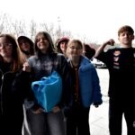 Grupa dzieci stoi przed biblioteką, trzymając koszyczki i prezentując różne pozy.