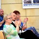 Grupa osób siedzących w sali i oklaskująca występ chóru.