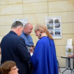 Trzy osoby w garniturach rozmawiają podczas uroczystości w pomieszczeniu z galeriami zdjęć na ścianie.