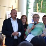 Mężczyzna w garniturze i kobieta przemawiają do publiczności podczas wydarzenia w bibliotece.