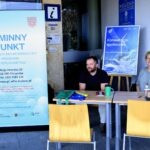 Dwóch mężczyzn siedzi za stolikiem podczas pikniku edukacyjnego związanego z Europejskim Dniem Bez Samochodu.