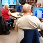 Uczestnicy zajęć siedzą przed komputerami w sali szkoleniowej.