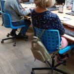 Uczestnik szkolenia siedzi przy stanowisku komputerowym z niebieskim krzesłem obrotowym.