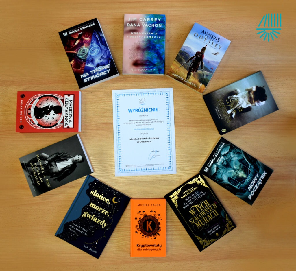 Na drewnianym stole ułożone są książki, certyfikat wyróżnienia oraz inne przedmioty związane z działalnością biblioteki.
