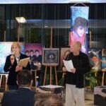 Mężczyzna trzyma kartkę, a kobieta prezentuje notatki przed wystawą obrazów inspirowanych zespołem The Beatles.
