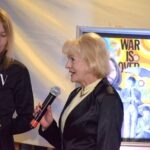 Kobieta trzyma mikrofon podczas wydarzenia związanego z wystawą inspirowaną zespołem The Beatles.