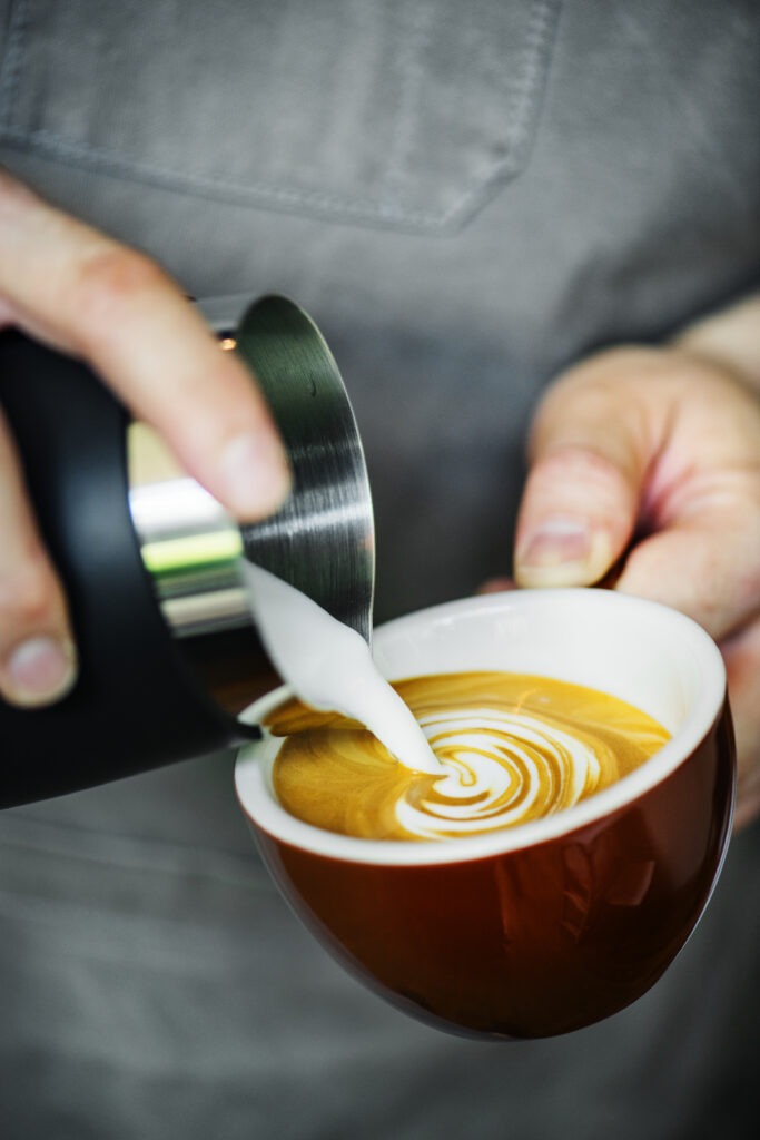 Barista tworzy wzór z mleka na powierzchni kawy w filiżance.