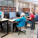Uczestnicy warsztatów pracują przy komputerach w sali bibliotecznej.