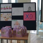 Na tablicy znajdują się dziecięce rysunki, a pod nią leżą pakiety z upominkami dla uczniów.